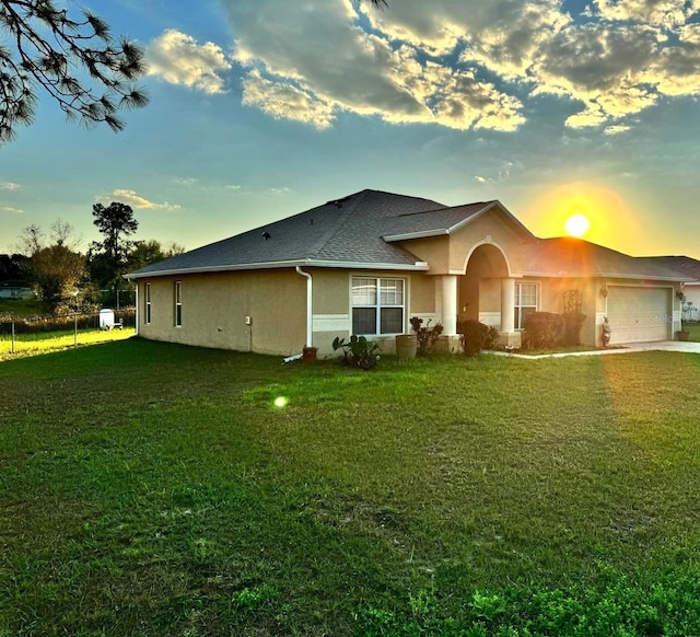 rear view of house with a garage, a shingled roof, driveway, a lawn, and stucco siding