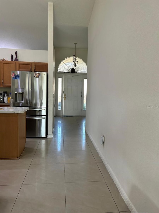 kitchen with light tile patterned floors, baseboards, light countertops, stainless steel refrigerator with ice dispenser, and brown cabinets