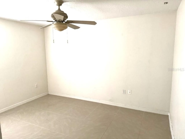 tiled empty room featuring a ceiling fan and baseboards