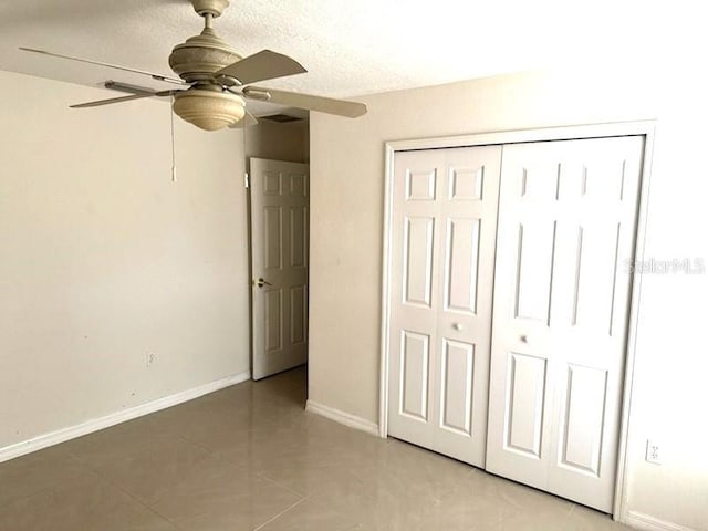 unfurnished bedroom with light tile patterned floors, a closet, ceiling fan, a textured ceiling, and baseboards