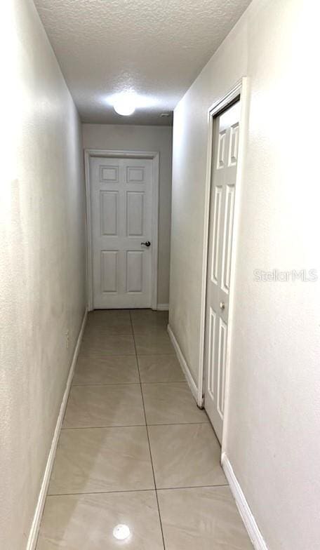 hall with light tile patterned flooring, a textured ceiling, and baseboards