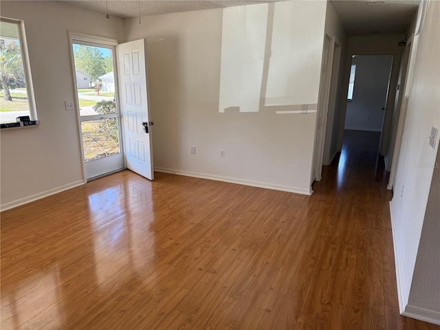 spare room featuring a textured ceiling, baseboards, and wood finished floors