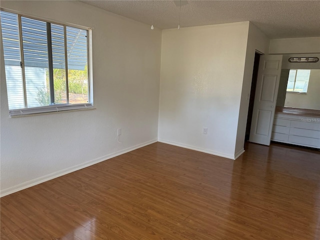 empty room with a textured ceiling, wood finished floors, and baseboards