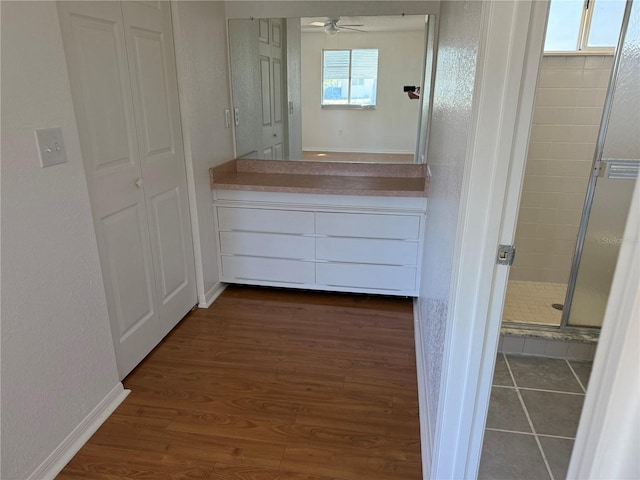 full bath featuring a textured wall, a shower stall, vanity, wood finished floors, and baseboards