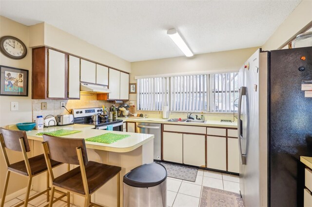 kitchen featuring light countertops, appliances with stainless steel finishes, a sink, a peninsula, and under cabinet range hood