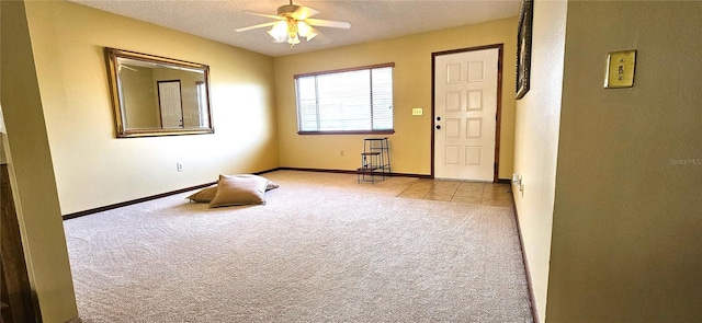 carpeted empty room with a ceiling fan, tile patterned flooring, a textured ceiling, and baseboards