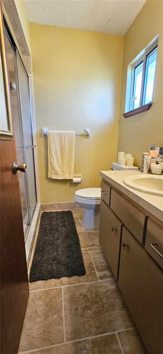 full bath with toilet, a shower stall, a textured ceiling, and vanity