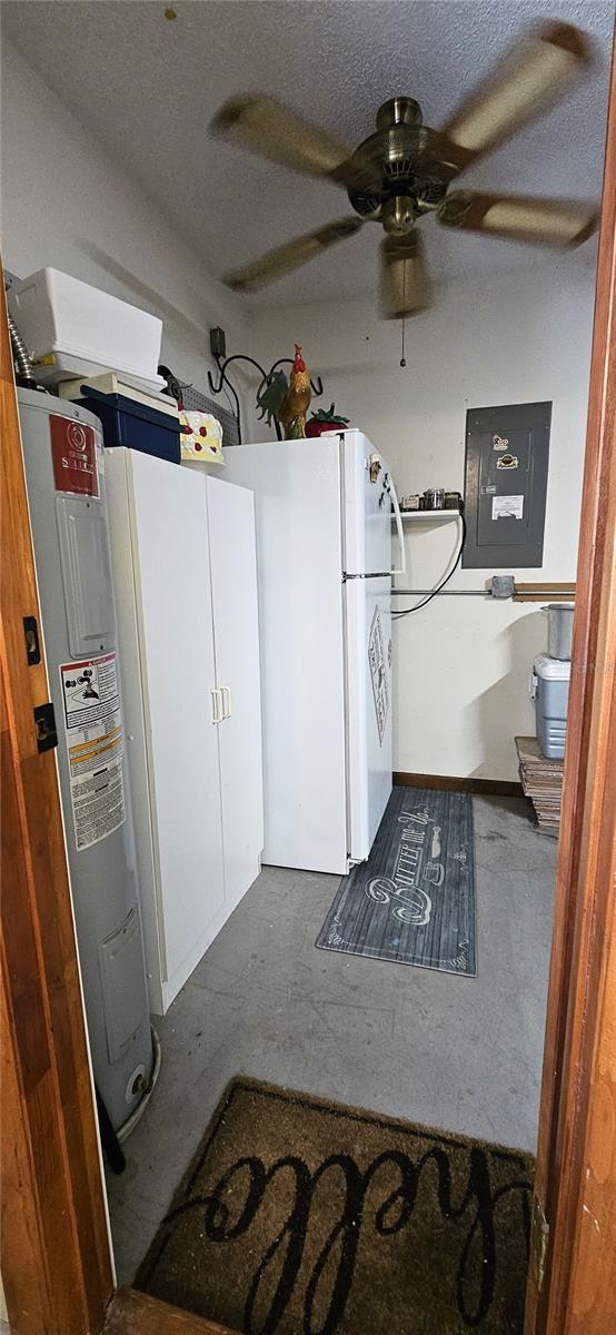 kitchen featuring concrete floors, electric panel, a textured ceiling, and electric water heater