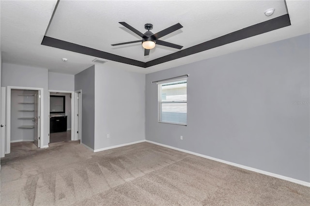 unfurnished bedroom with a tray ceiling, light colored carpet, visible vents, a textured ceiling, and baseboards