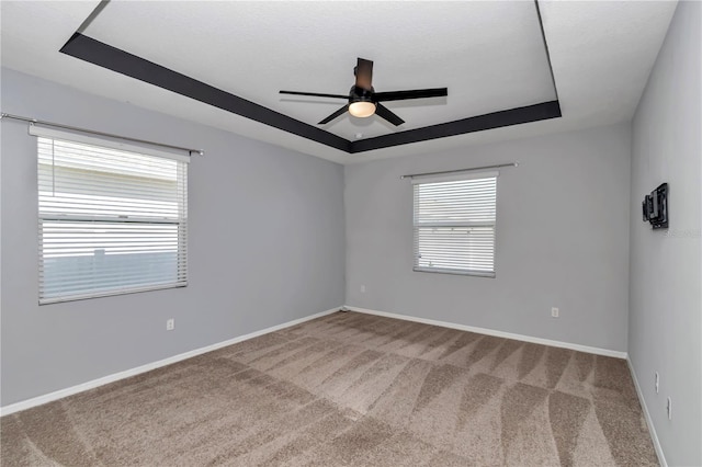 carpeted empty room featuring baseboards, a tray ceiling, and a ceiling fan