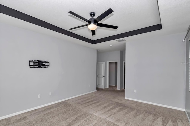 spare room with ceiling fan, visible vents, baseboards, a tray ceiling, and carpet