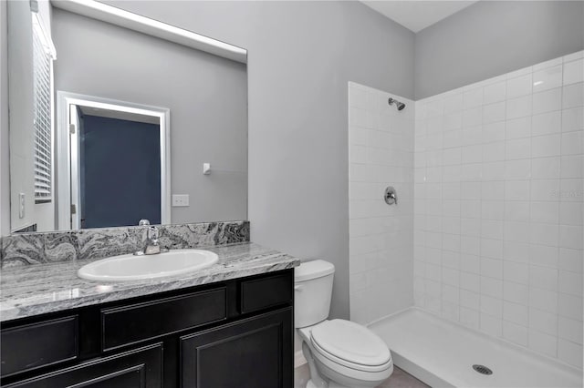 bathroom with toilet, a tile shower, and vanity