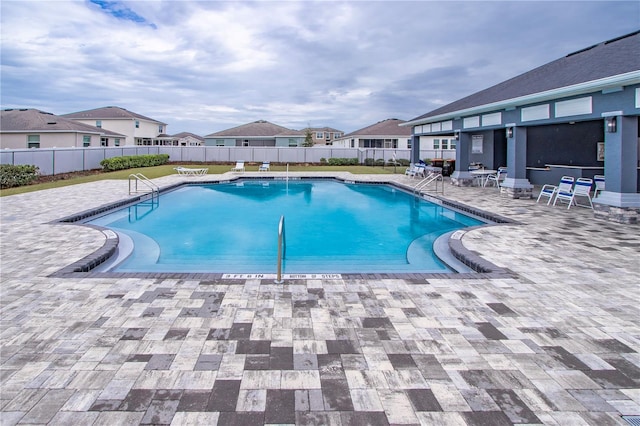 community pool with a residential view, a patio area, and fence