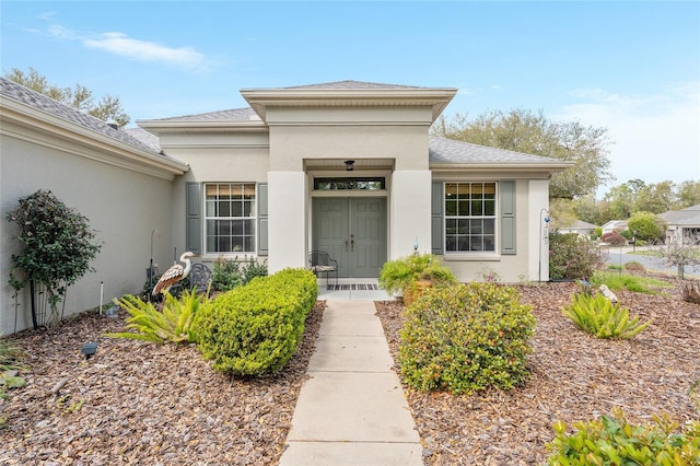 property entrance featuring covered porch, a shingled roof, and stucco siding