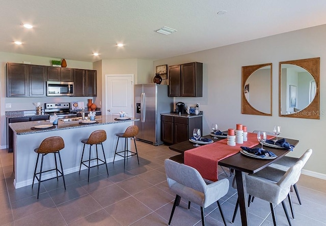 kitchen featuring a breakfast bar area, visible vents, appliances with stainless steel finishes, dark brown cabinetry, and an island with sink