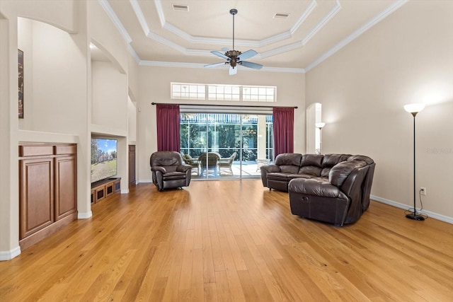 living area featuring visible vents, a raised ceiling, a ceiling fan, ornamental molding, and light wood-type flooring