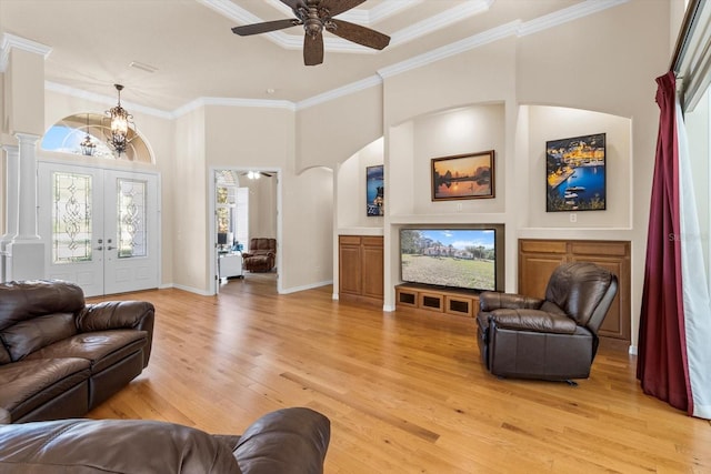 living area featuring baseboards, a towering ceiling, crown molding, light wood-type flooring, and ceiling fan with notable chandelier