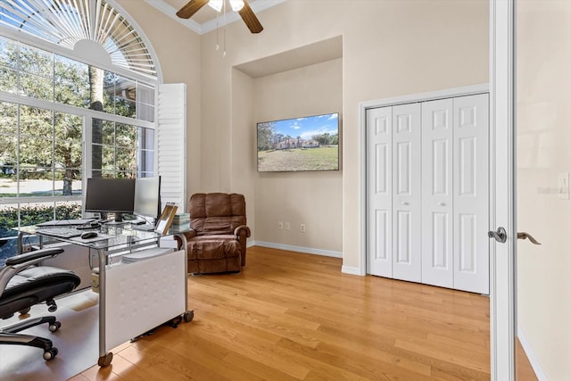 office space with crown molding, a high ceiling, ceiling fan, wood finished floors, and baseboards