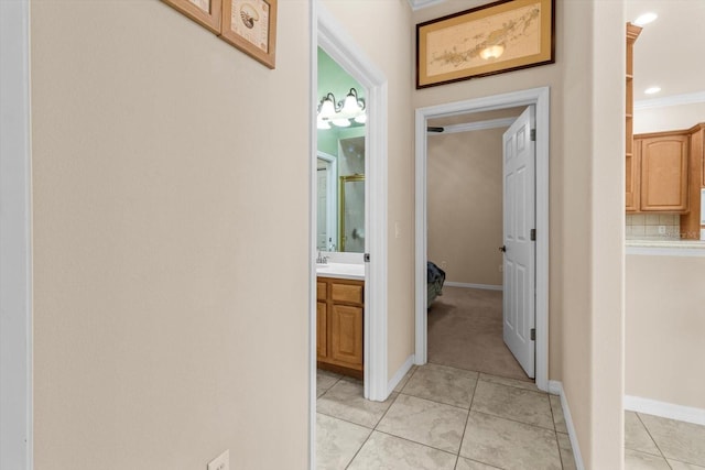 hallway featuring light tile patterned floors, ornamental molding, and baseboards