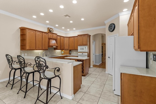 kitchen featuring white appliances, arched walkways, a kitchen breakfast bar, a peninsula, and open shelves