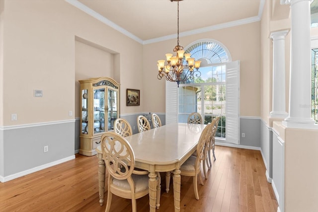 dining space featuring crown molding, decorative columns, an inviting chandelier, light wood-style floors, and baseboards