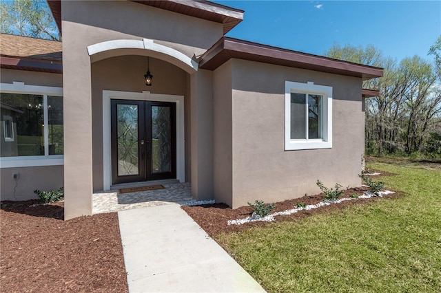 property entrance with a yard, french doors, and stucco siding