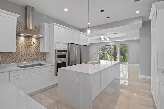 kitchen featuring stainless steel appliances, tasteful backsplash, white cabinetry, a sink, and wall chimney range hood