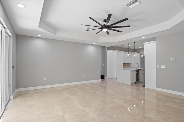 unfurnished living room featuring a raised ceiling, visible vents, a ceiling fan, a sink, and baseboards