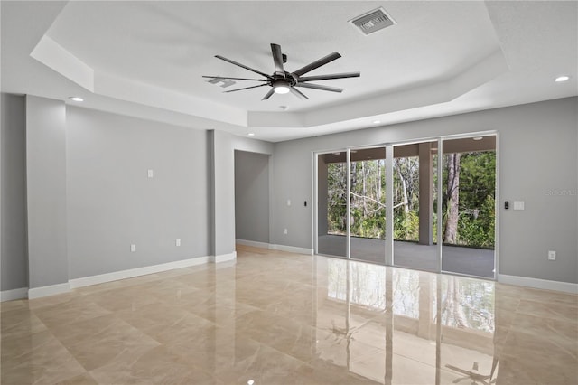 spare room with a ceiling fan, a tray ceiling, visible vents, and baseboards