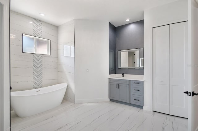 full bathroom featuring baseboards, marble finish floor, vanity, a freestanding tub, and recessed lighting