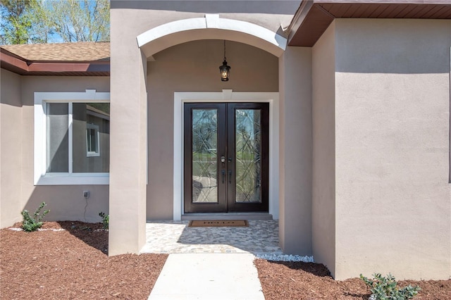 doorway to property featuring a shingled roof, french doors, and stucco siding