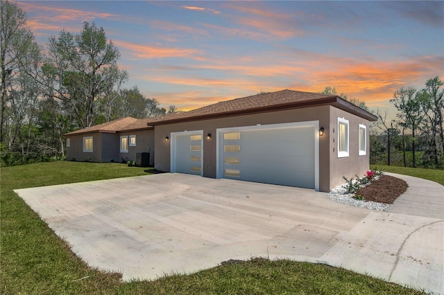 view of front of house featuring driveway, an attached garage, central air condition unit, a front lawn, and stucco siding