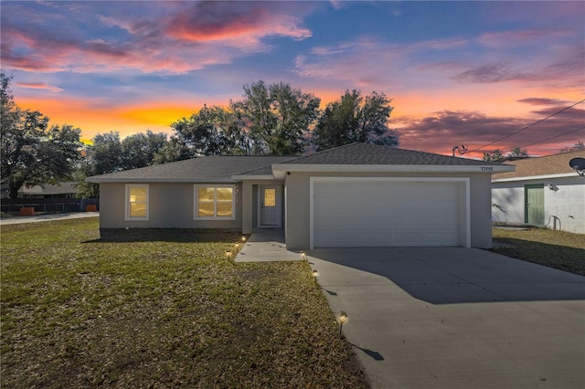 single story home featuring a garage, concrete driveway, a front lawn, and stucco siding