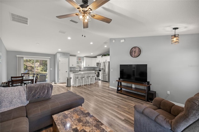 living room featuring vaulted ceiling, light wood-style flooring, visible vents, and baseboards