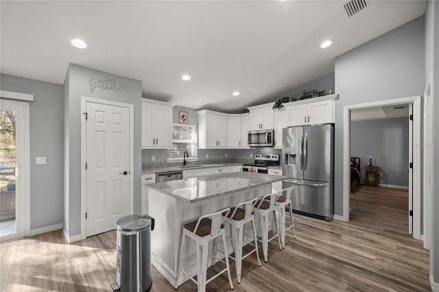 kitchen featuring visible vents, appliances with stainless steel finishes, a center island, white cabinetry, and a sink