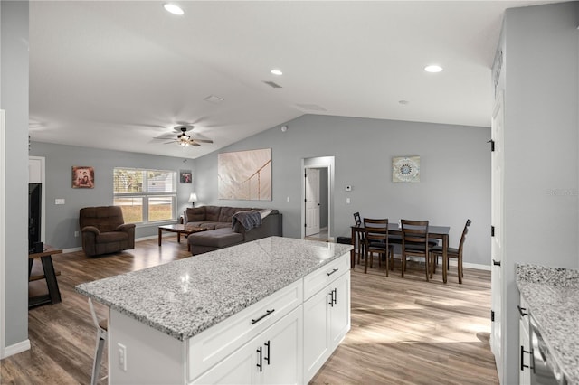 kitchen with white cabinets, lofted ceiling, light wood-style flooring, a kitchen island, and light stone counters