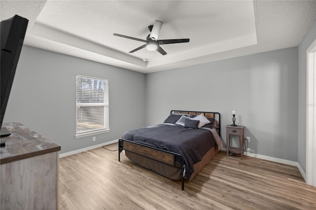 bedroom with light wood finished floors, baseboards, and a raised ceiling