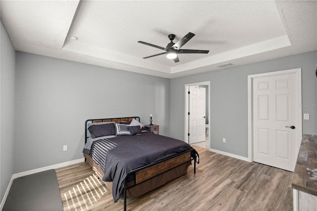 bedroom featuring baseboards, a tray ceiling, and wood finished floors