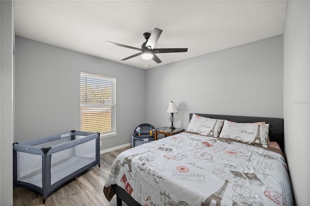 bedroom featuring ceiling fan, a textured ceiling, baseboards, and wood finished floors