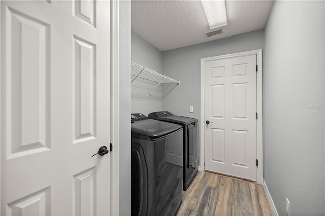 clothes washing area with laundry area, light wood finished floors, visible vents, washing machine and clothes dryer, and a textured ceiling