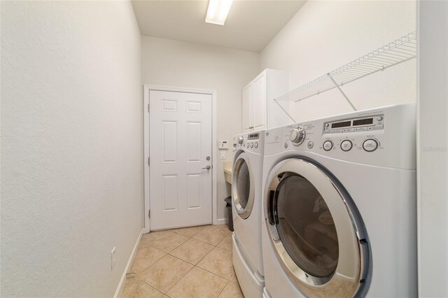 laundry room featuring washing machine and dryer, cabinet space, baseboards, and light tile patterned floors