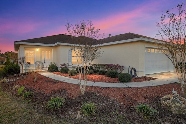 property exterior at dusk with stucco siding, a shingled roof, concrete driveway, covered porch, and an attached garage