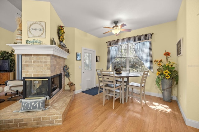 dining area featuring a brick fireplace, ceiling fan, baseboards, and wood finished floors