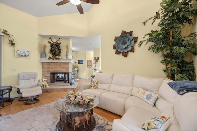 living room with lofted ceiling, a brick fireplace, ceiling fan, and wood finished floors