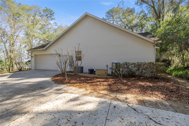 view of home's exterior with a garage, driveway, cooling unit, and stucco siding