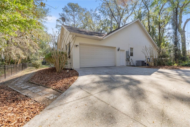 view of side of home featuring central AC unit, an attached garage, fence, concrete driveway, and stucco siding