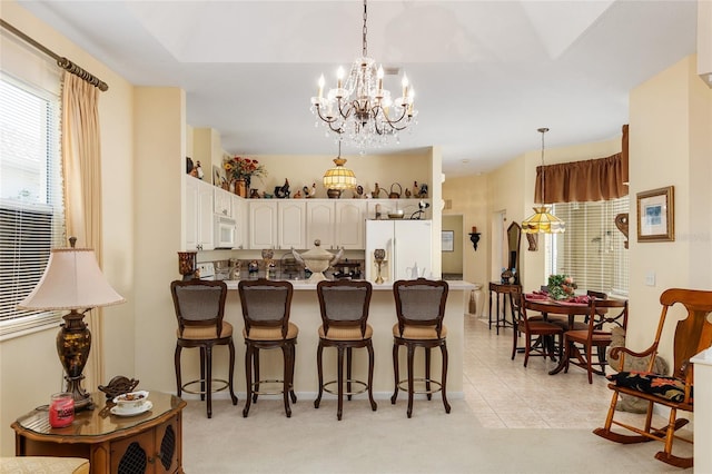 kitchen featuring white appliances, white cabinets, a peninsula, a kitchen bar, and pendant lighting