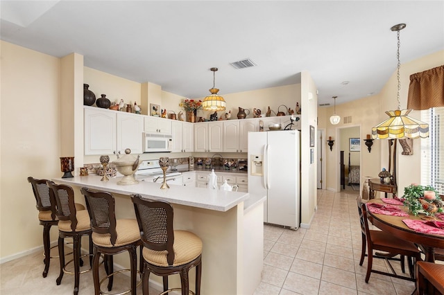 kitchen featuring white appliances, visible vents, white cabinets, a breakfast bar, and a peninsula