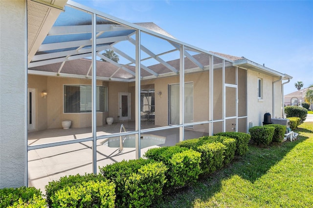 back of property with glass enclosure, a lawn, a patio, and stucco siding