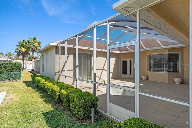 rear view of property with stucco siding, a lawn, glass enclosure, a patio area, and fence